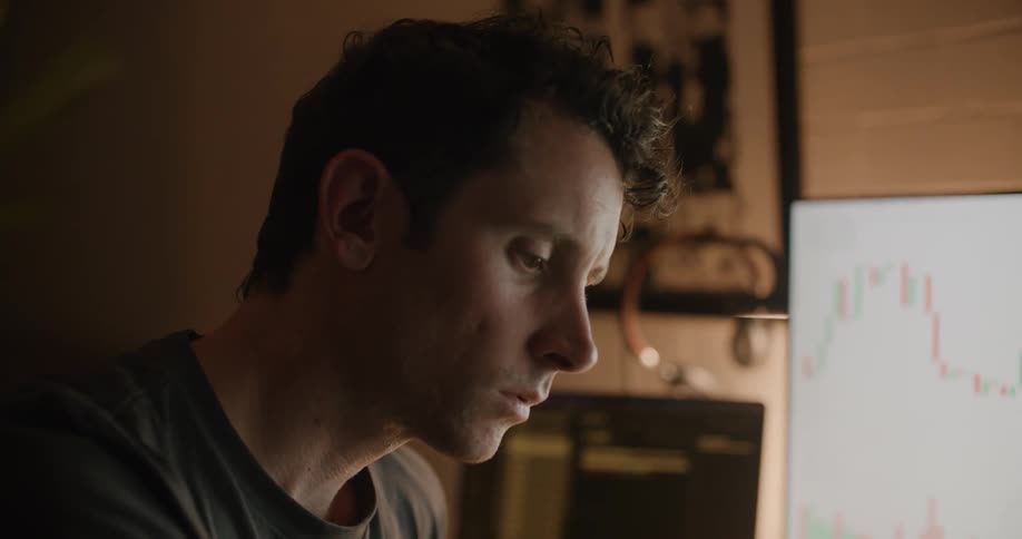 Man sitting at the desk writing down on his notepad while looking at the monitor screen