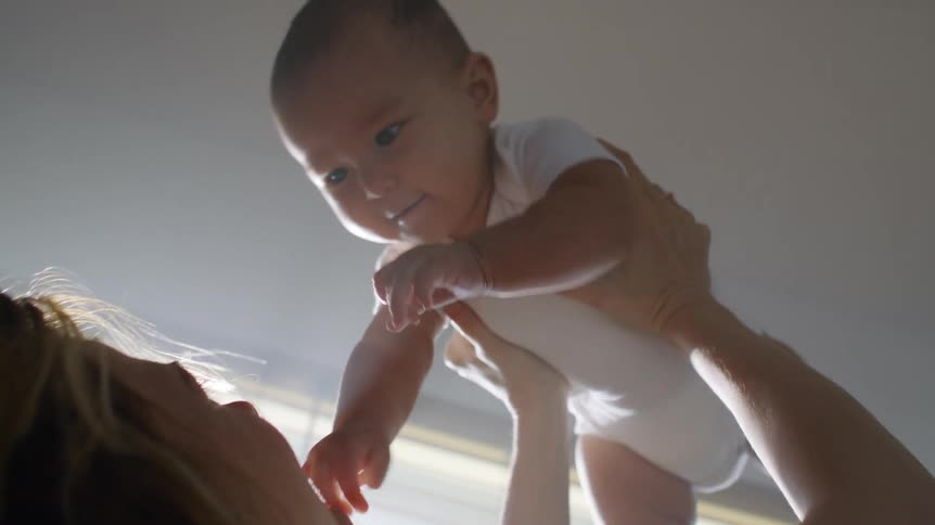 Mother with wavy hair holds up baby son playing together