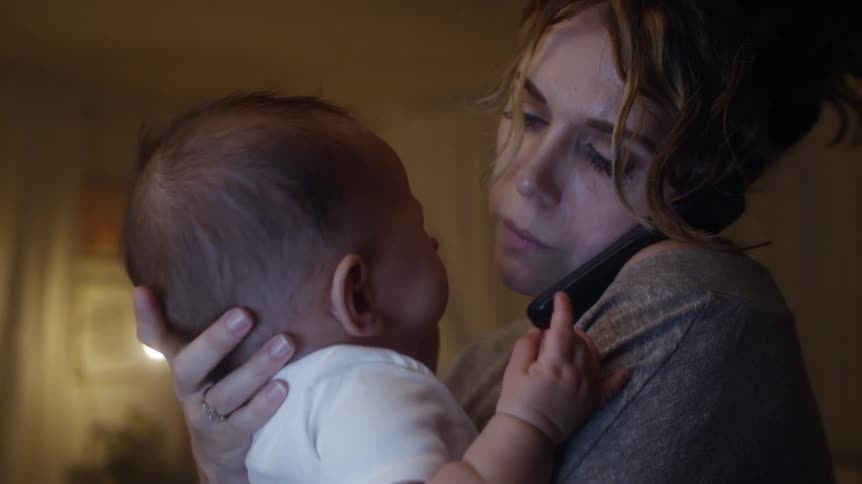 A mother rocks her baby as she talks on the cell phone