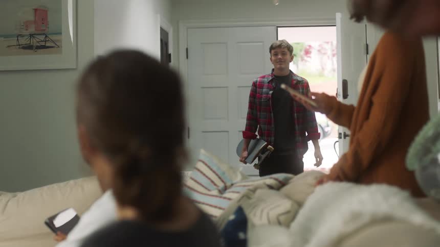 Young man bursts into room excitedly then stops dejected to see several people already in living room with their devices