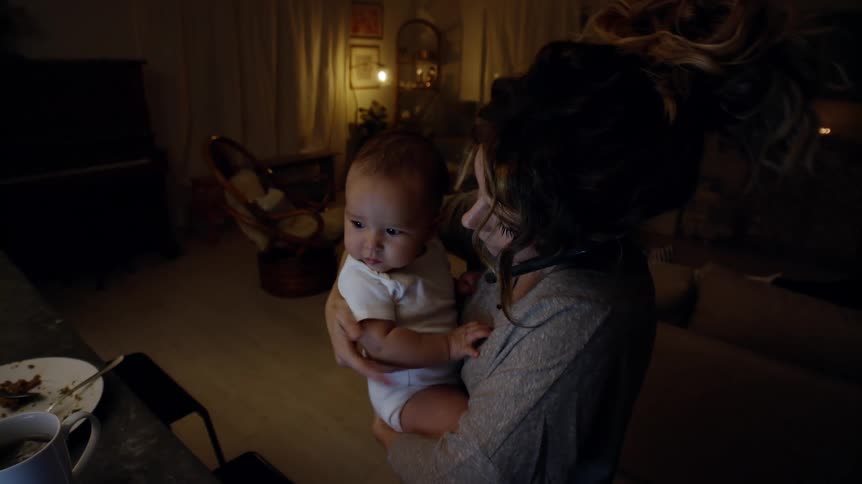 Mother standing inside her house holding her baby while talking to the phone