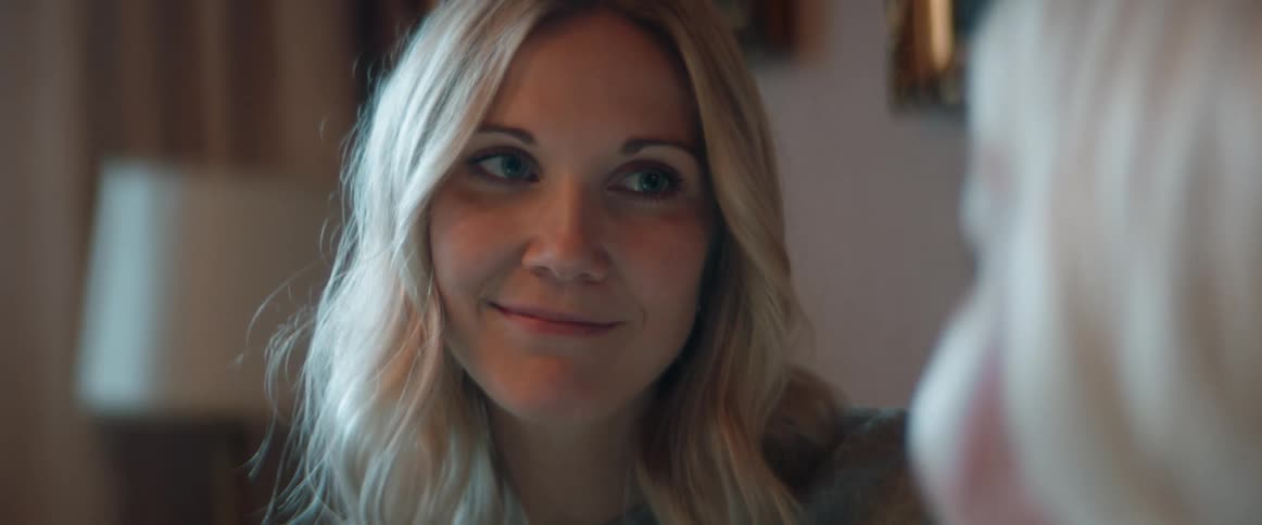 A woman with long blond hair is smiling affectionately at an older woman near her