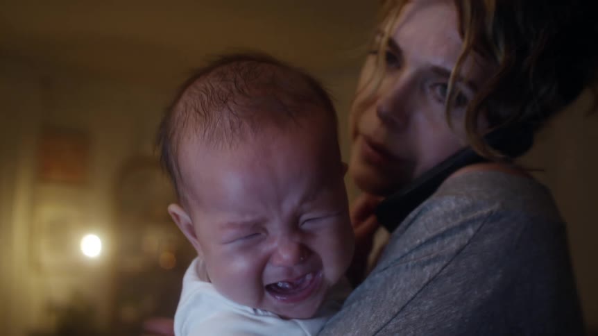 A woman struggles to calm her baby while holding him and talking on the phone