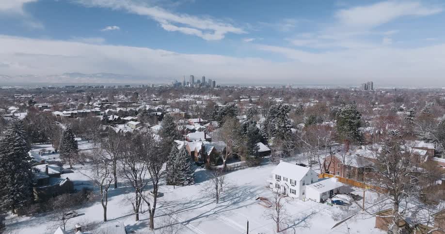 Aerial view of snow covered suburban neighborhood with skyline in the distance