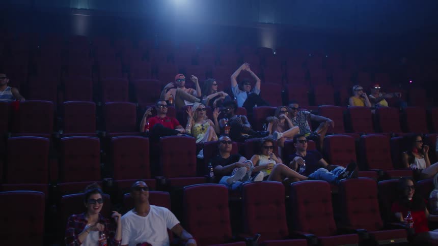 A group of people in a movie theater lean back and put on 3D glasses