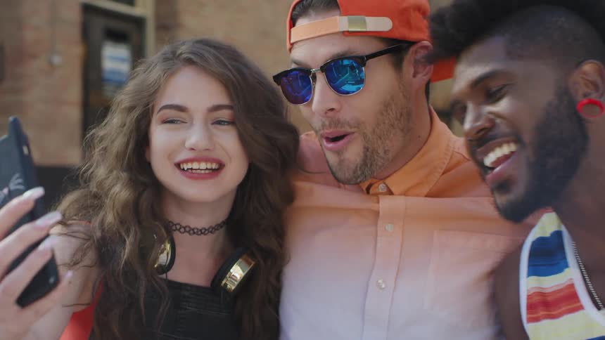 Three young friends standing outdoors wearing different kind of clothings video calling someone on a smartphone