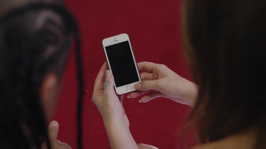 Woman holding a smartphone in front of her and of another person sitting next to her