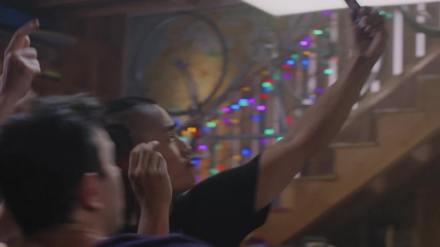 Three young friends dancing and partying inside a house while filming themselves on a smartphone