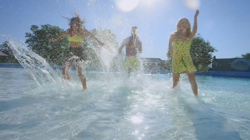 Three young people dance and splash in a pool