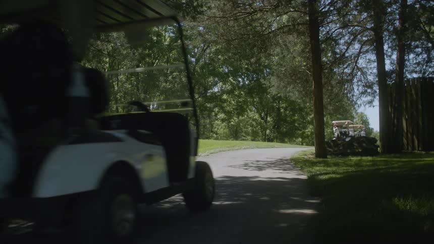 Golfers drive their carts down a paved road on a golf course