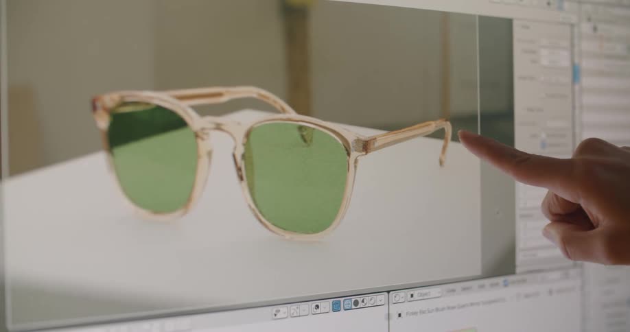 A woman touches her computer monitor displaying a pair of sunglasses being designed