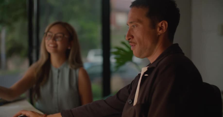 Woman holds a cellphone up near a monitor and smiles as she talks to a man sitting next to her