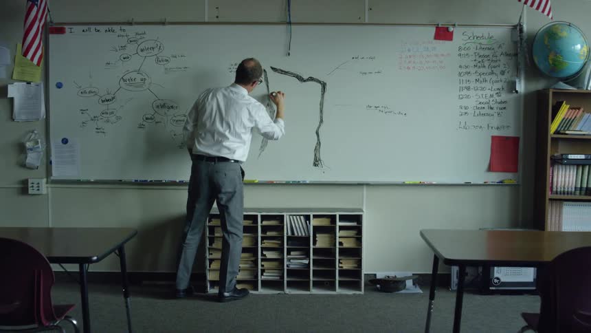 Teacher standing on an empty classroom drawing on the whiteboard and preparing his class