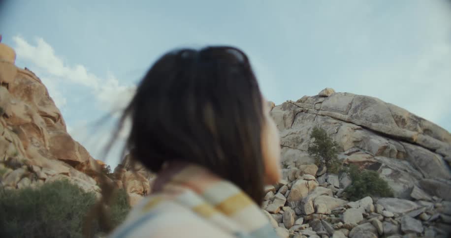 Hispanic woman standing outdoors next to a rock formation wrapped in a colorful blanked