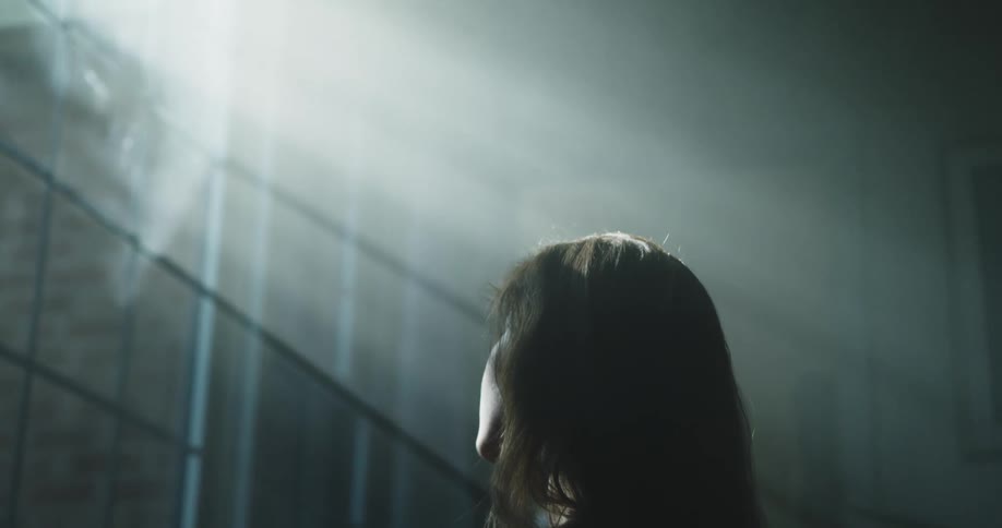 A woman stands in front of a blacked out window