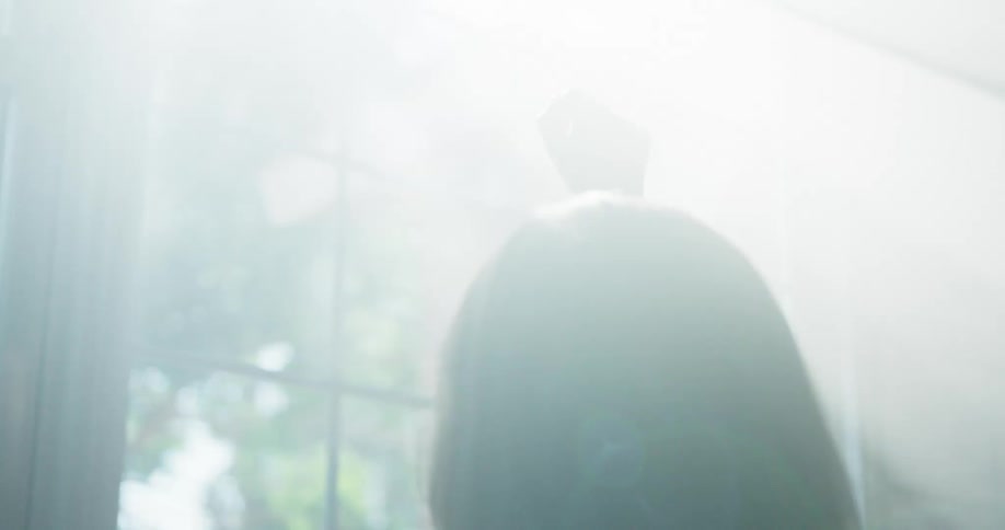 A woman holding a pendant necklace up high at a window catching the sunlight
