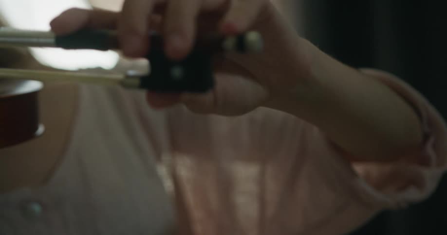Woman with white shirt and brown hair plays violin moving the bow across the strings