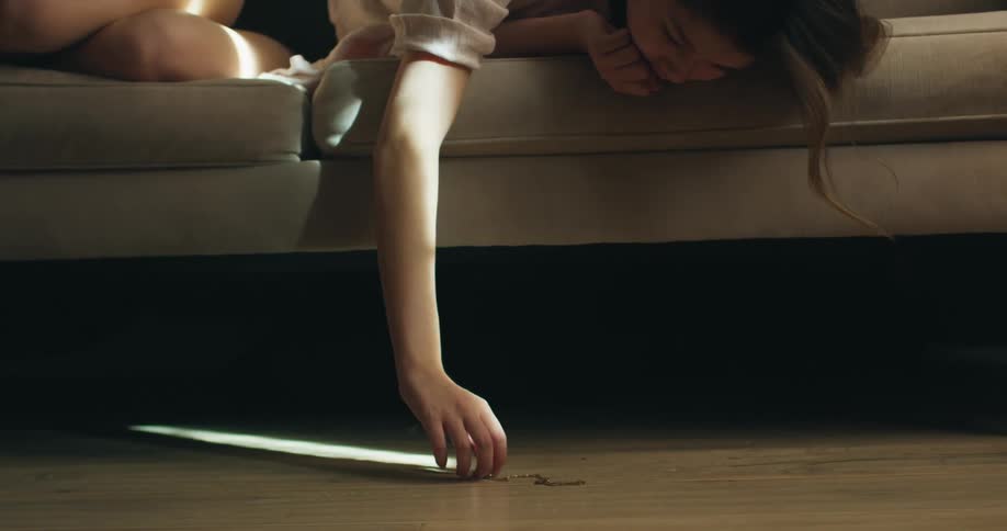 Young woman lying down in the couch and reaching her arm to pick up a necklace from the ground