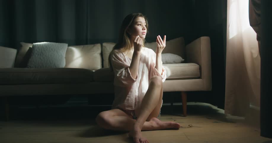 Young woman sitting in the floor in front of a couch picking up a wireless earphone and putting on her ear