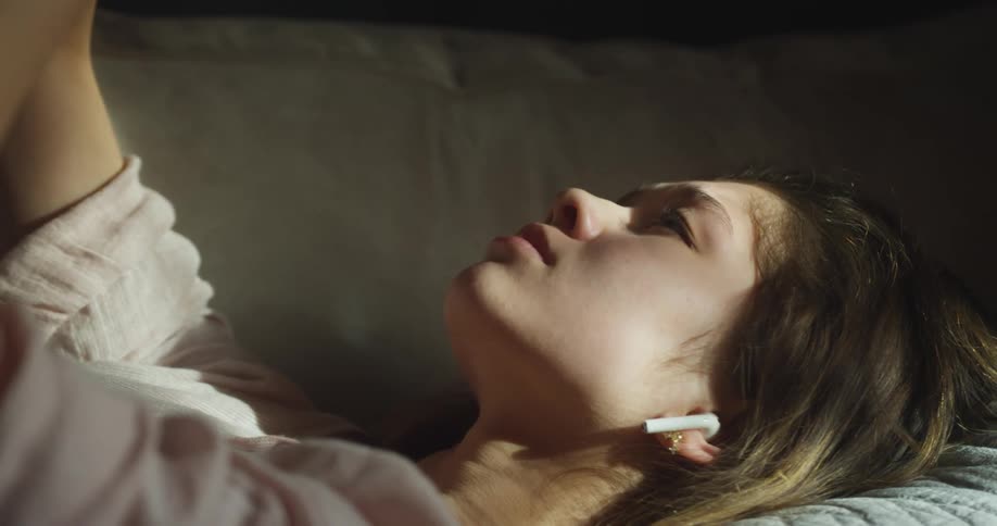 White woman wearing a wireless earphone lying down with her arms up