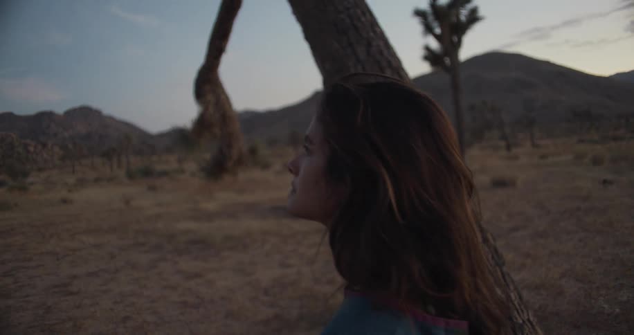 A woman sleeping alone in the desert sits up and looks around as the sun rises in the sky