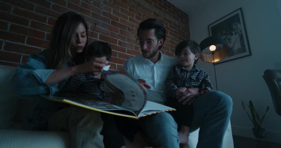 Mother father and two kids sitting on the couch and reading a book