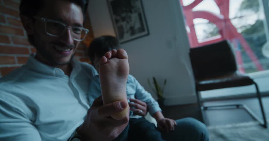 A father holds his young son in his knee and rubs his foot