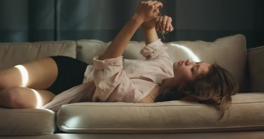 A young woman lies on a couch and lifts a necklace over her head