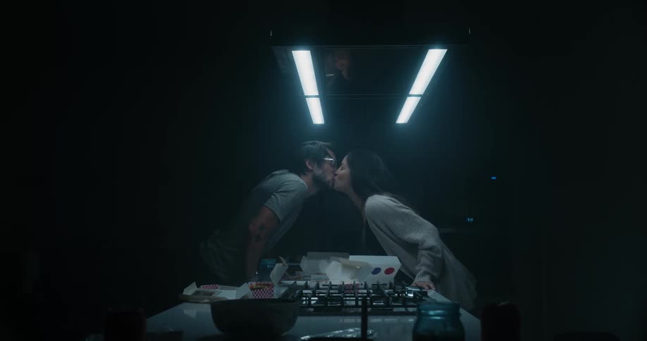 Couple standing on opposite sides of kitchen island lean forward to kiss