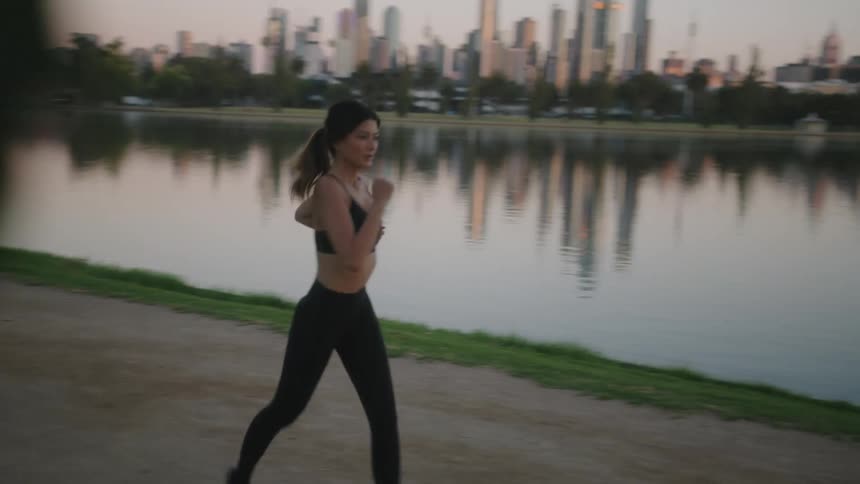 Woman jog along trail across water from downtown city skyline