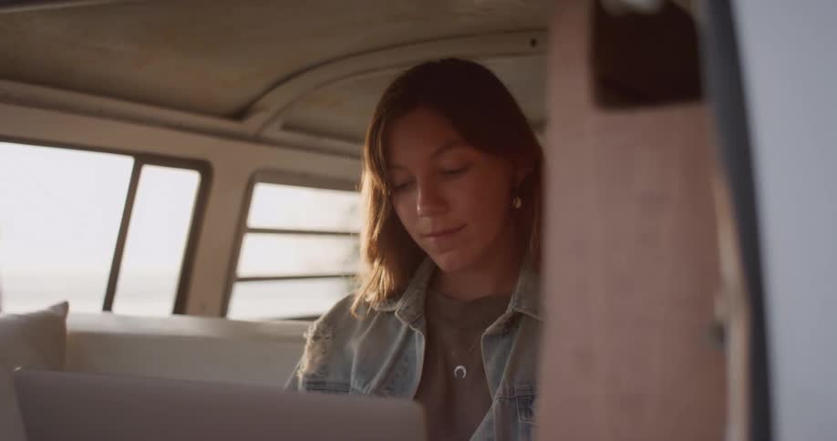 A young woman uses a laptop while sitting inside a large vehicle during the day