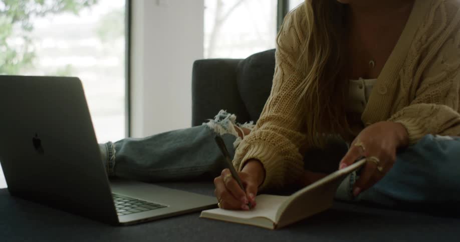 A woman writes in her notebook and types on her laptop