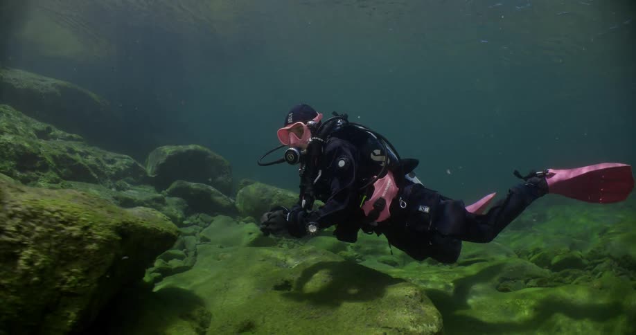 Scuba diver drifts over seafloor passing boulders