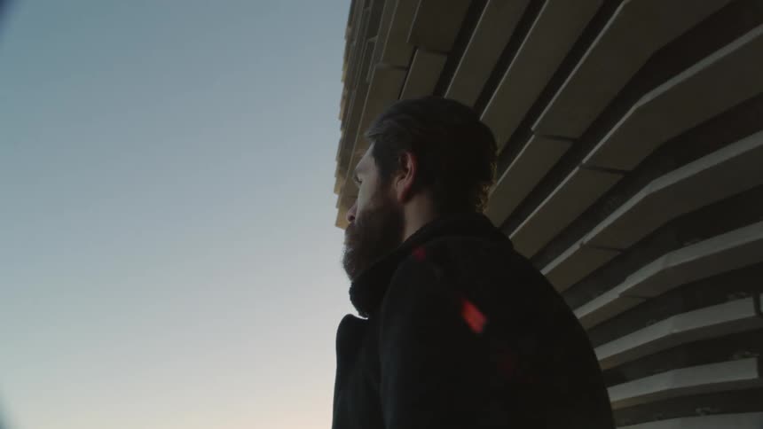 Bearded man emerges from near building and looks toward horizon on sunny day