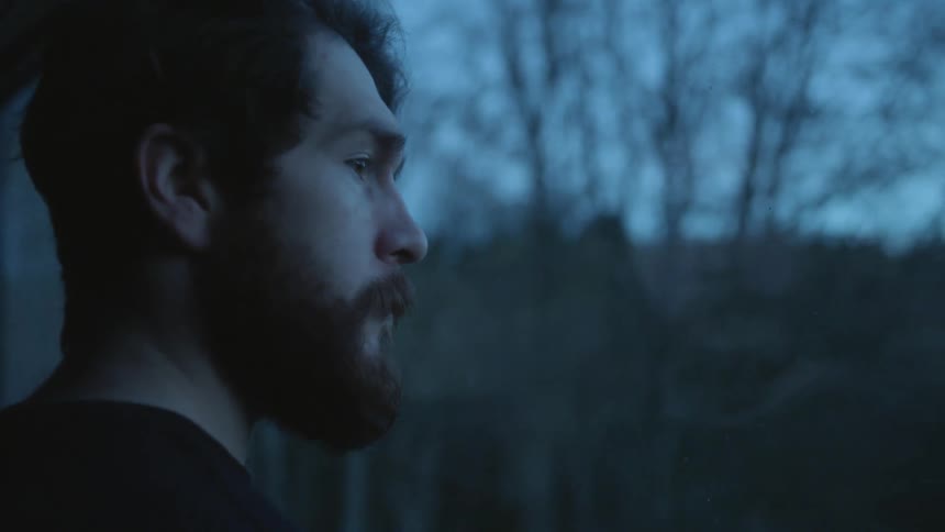Window reflects image of man standing looking out at woods