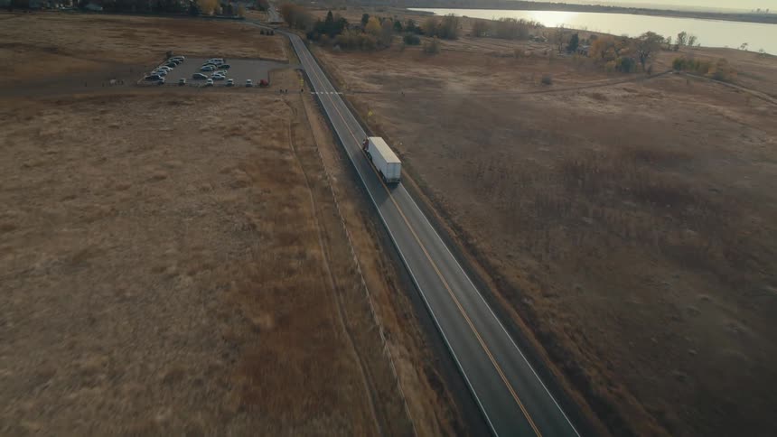Three people stand on the side of a road as a shipping truck drives past