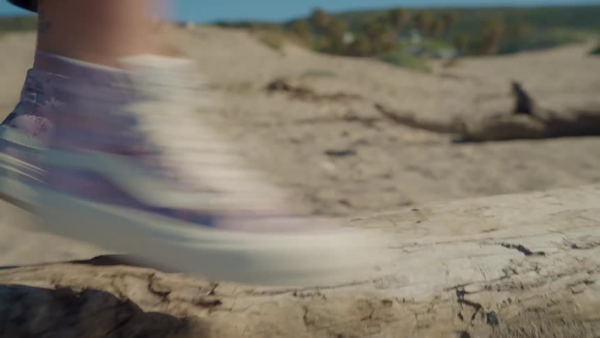 A woman uses a fallen tree trunk on the beach as a balance beam