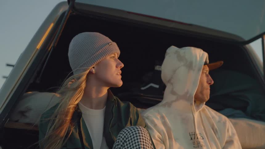 A man sitting next to his girlfriend smiles as he pulls his hood up