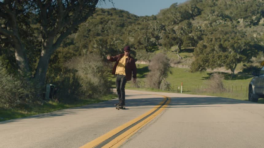 A skateboarder rides down a long country road