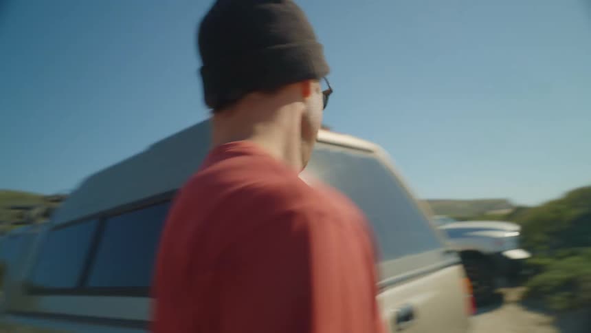 Man gets out of vehicle and the pulls out surfboard and places it on sand with ocean in background