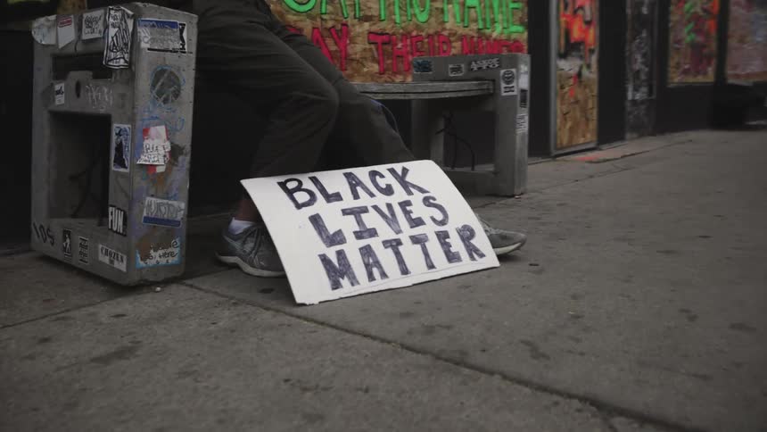 Black lives matter sign on the foot of a young man sitting on a bench in the city street