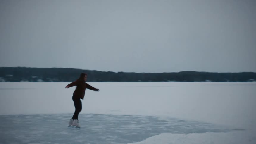 Young woman ice skating over a frozen lake in the snow covered field at winter