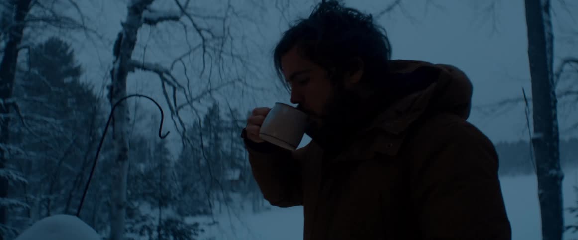 Young bearded man drinking a hot beverage near a snow covered forest at evening
