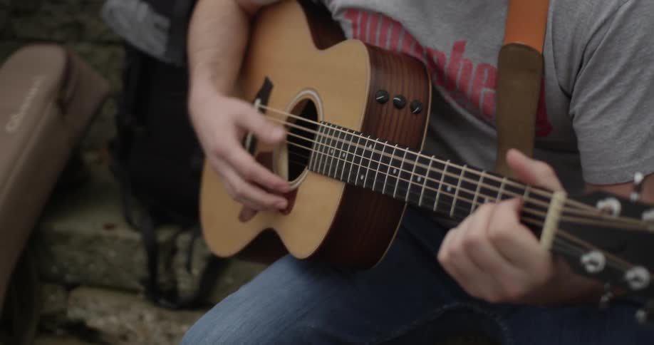 A man strums a guitar while sitting on some steps