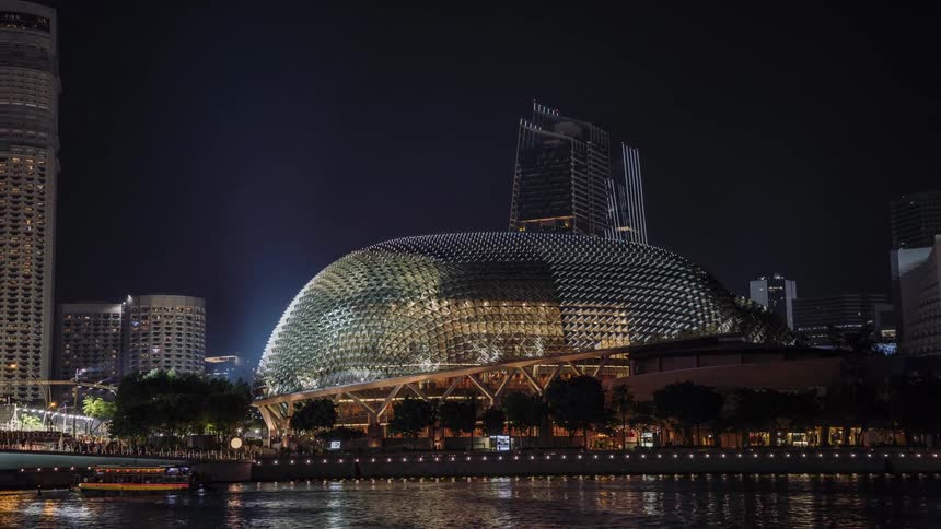 Boat travels down the river next to the city buildings at night