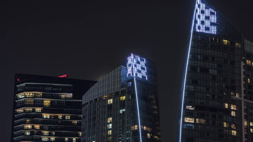 The partial moon rises behind the buildings