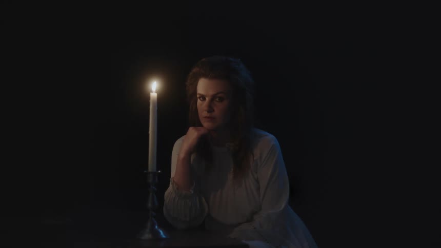 A woman sits by a table with a lit candle and thinks