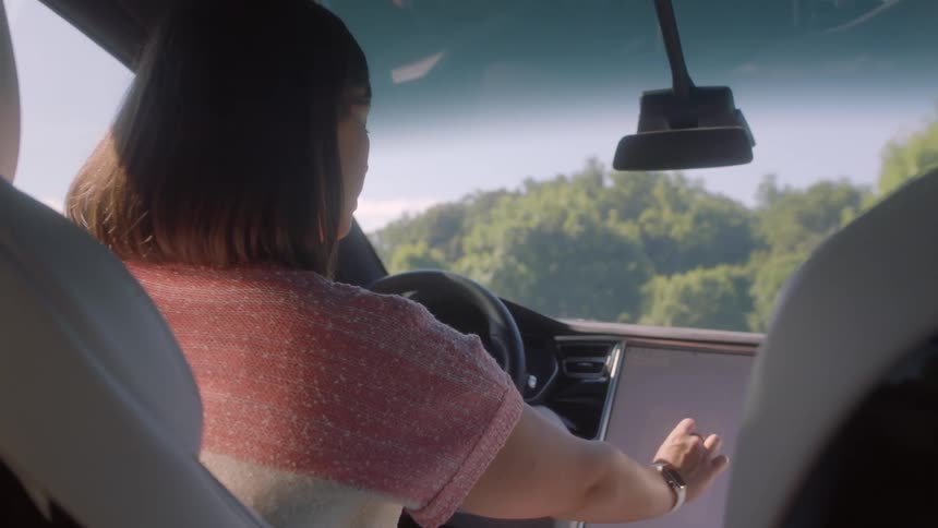 Woman with pink blouse sits in car using tablet