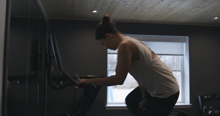 Woman getting on stationary bike and begins pedaling in her home gym