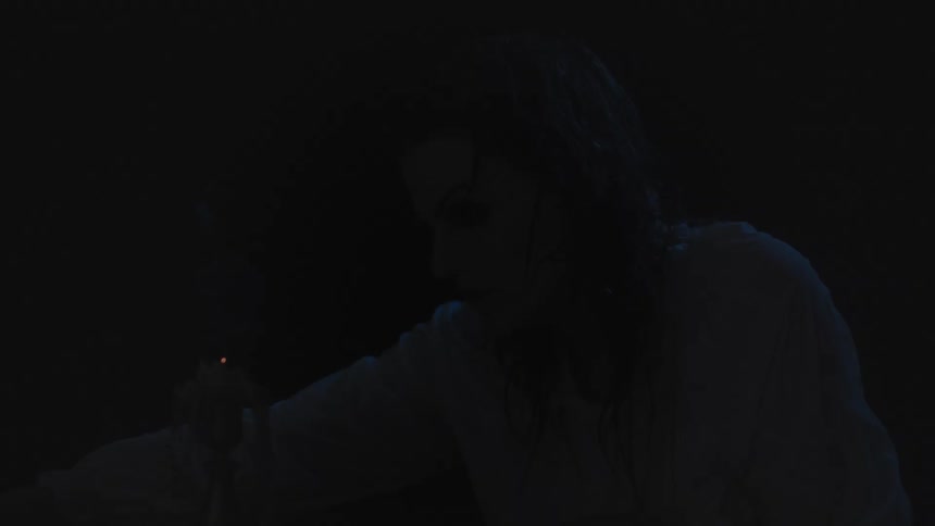 Woman wearing a white gown sitting in front of a candle going out inside a room at night